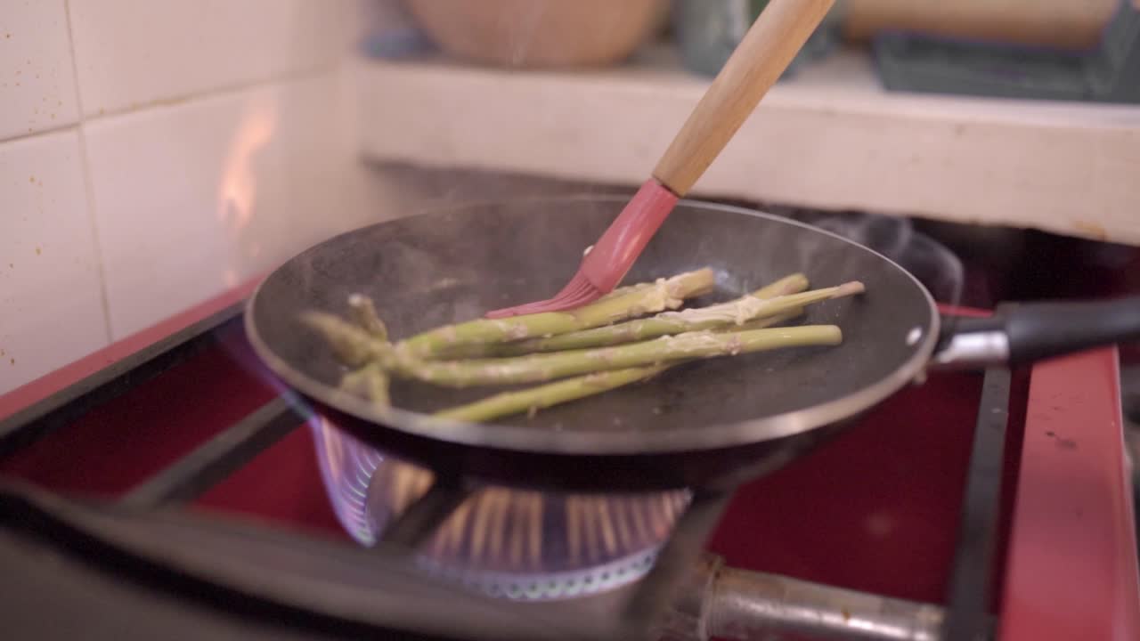 Unrecognizable chef frying asparagus in kitchen