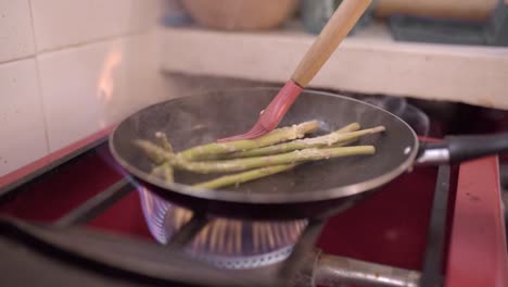 unrecognizable chef frying asparagus in kitchen