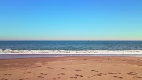 drone pov of an empty sand beach at daytime, moving into the water