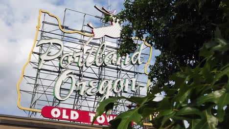 HD-Panning-and-trucking-right-to-left-past-trees-to-reveal-the-Portland-Oregon-Old-Town-sign-with-the-Old-Town-water-tower-peeking-through-and-out-from-sign-with-mostly-cloudy-sky