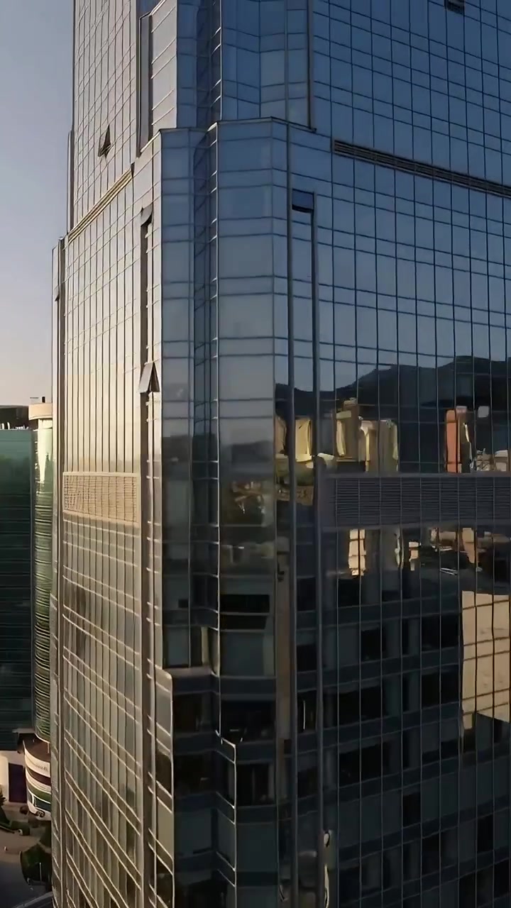 Vídeo vertical: Drone subindo capturando torre espelhada no centro da cidade, revelando reflexos na estrada