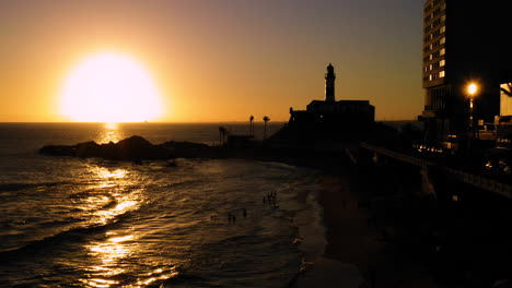 Aerial-view-of-Farol-da-Barra,-the-sea-and-the-neighborhood-around,-at-sunset,-Salvador,-Bahia,-Brazil