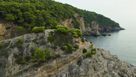 Kalamota-Island,-Adriatic-Sea,-Croatia---The-Stunning-Vista-of-the-Island's-Rugged,-Vegetated-Cliffs-and-Clear-Blue-Waters---Aerial-Pullback-Shot