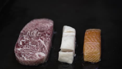 beef steak, salmon and cord fish being grilled on black flat satake frying table - close-up shot
