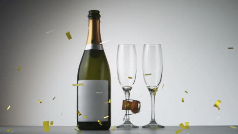 confeti dorado cayendo sobre una botella de champán y dos copas de champán contra un fondo gris