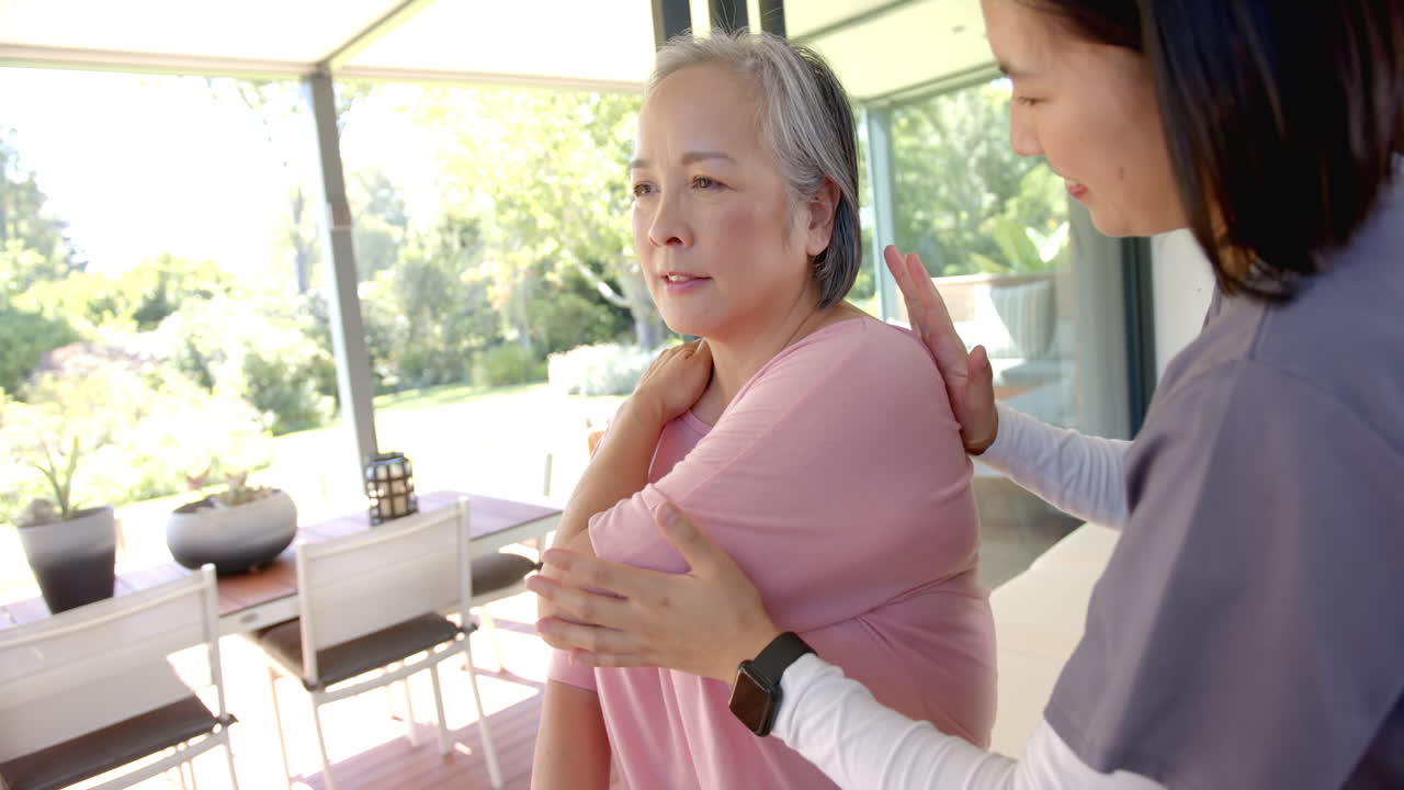 Assisting senior asian woman with shoulder exercise, physiotherapist at home