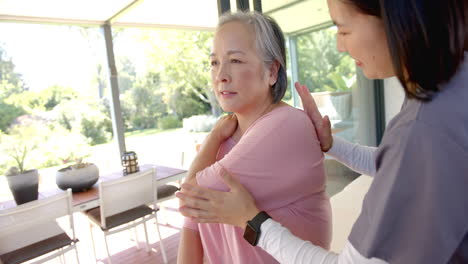 assisting senior asian woman with shoulder exercise, physiotherapist at home