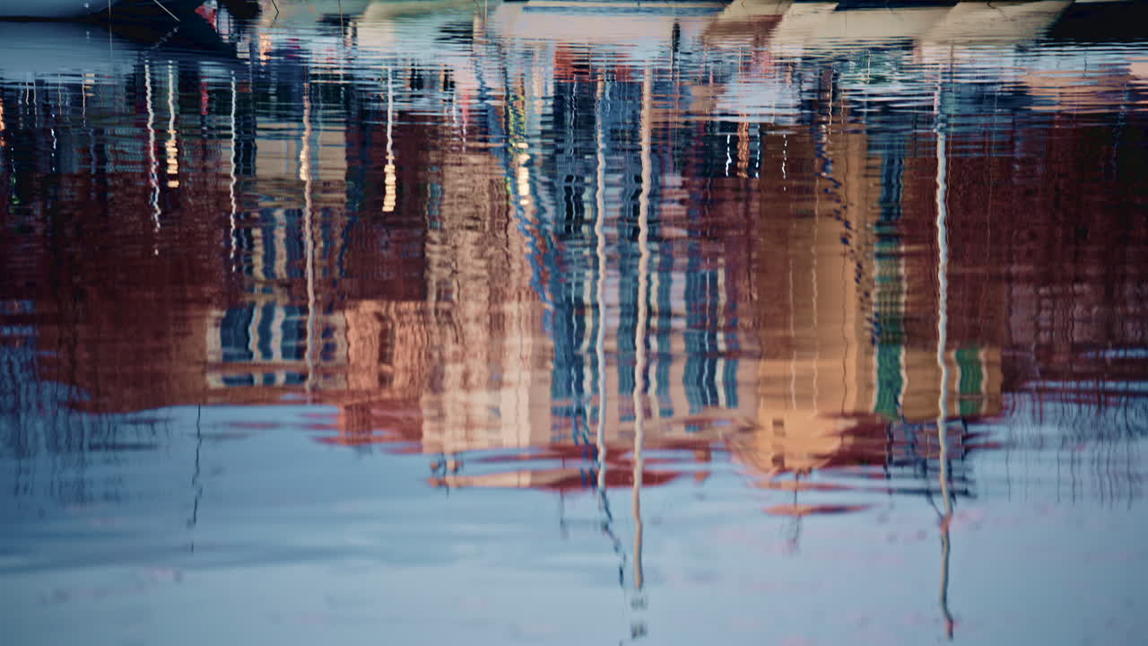 Detailed shot of distorted reflections of buildings and boats on gently moving harbor water