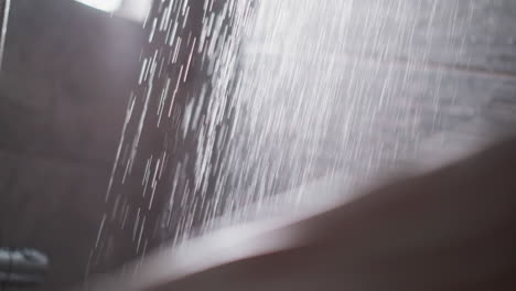 shower water and blurry woman touching bare leg in bathroom closeup. fresh spraying jets fall down while lady takes bath in washroom. beauty routine