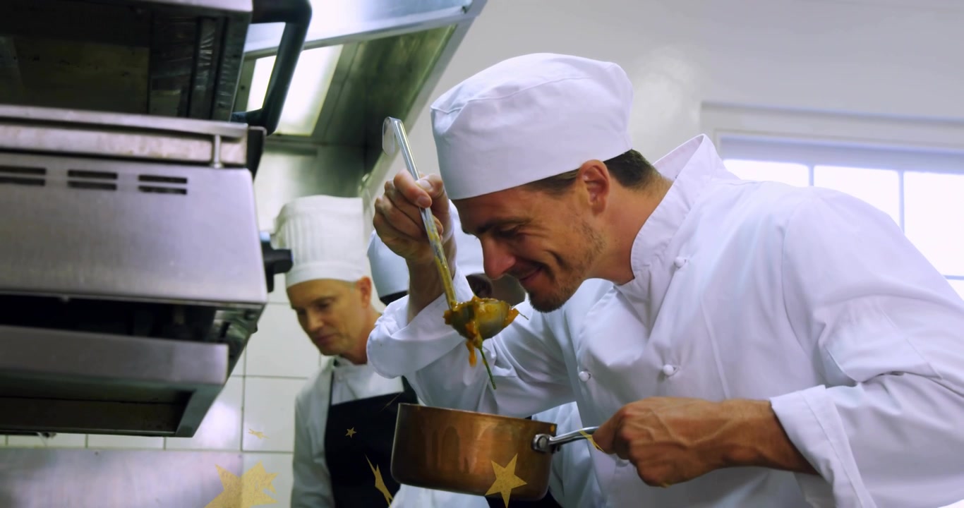 Capo chef che preleva la salsa per il controllo del condimento mentre il team impiattava i piatti e mescola le pentole in cucina.