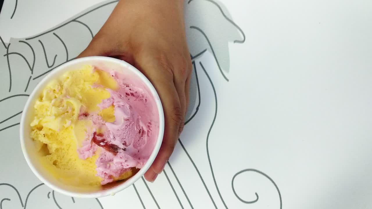 Primo piano di qualcuno che preleva palline di gelato multicolore dal contenitore per mangiarle
