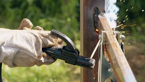 close view worker connects plank to fence with welding tool