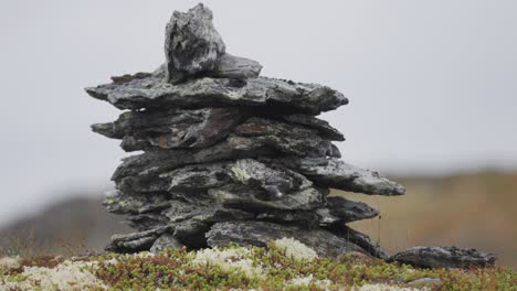 a stone cairn made of dark jagged stones on a moss-covered rocky terrain