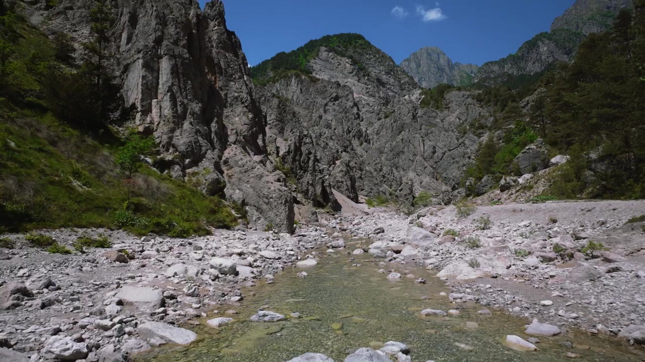 Acqua cristallina di un fiume alpino che scorre su ghiaia con montagne sullo sfondo, Dolomiti Friulane, Italia.