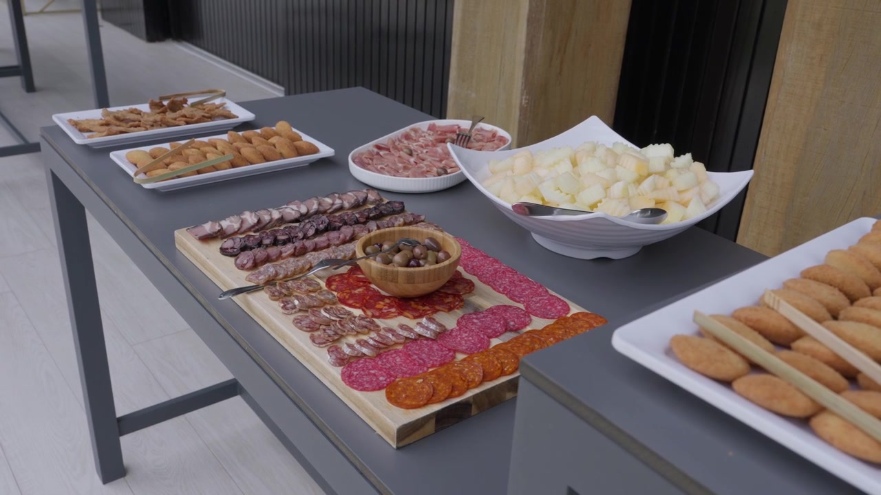 Tagliere di salumi con chorizo, salame, olive, formaggio e stuzzichini fritti su un lungo tavolo.