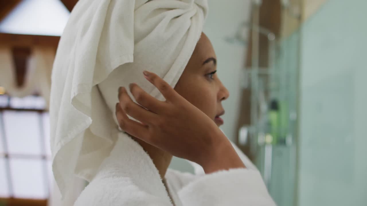 Mixed race woman wearing bathrobe looking at mirror