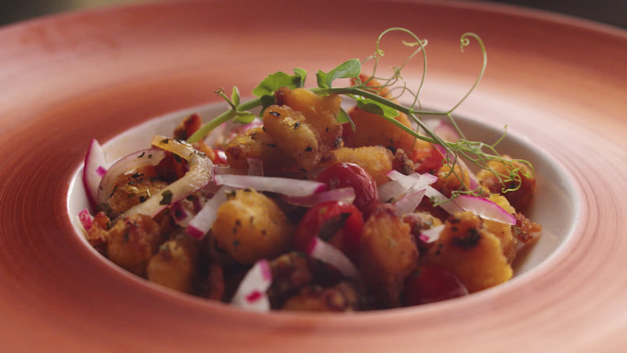A gourmet potato dish with red onions, cherry tomatoes, and microgreens
