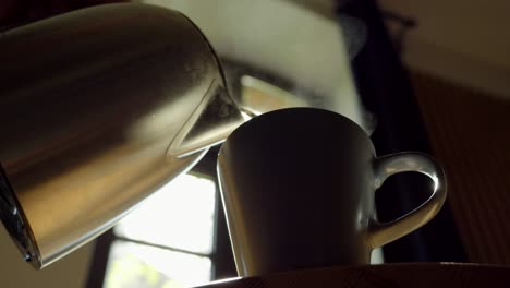 vertiendo agua hirviendo de una tetera de metal en el café contra el telón de fondo de la luz del sol que fluye a través de una ventana de madera