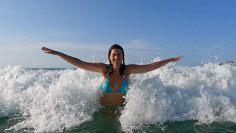 beautiful smiling active woman with blue bikini and arms wide open waiting big sea waves splashing on her