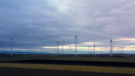 Langer,-Langsamer-Kranschuss-Von-Einer-Drohne,-Die-über-Die-über-Das-Feld-Verstreuten-Windkraftanlagen-Hinwegfliegt