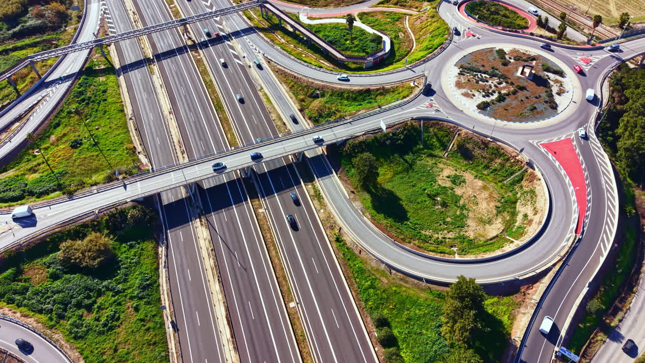 Traffic flows through an intersection with multiple roads in a green area under a clear sky during daylight hours