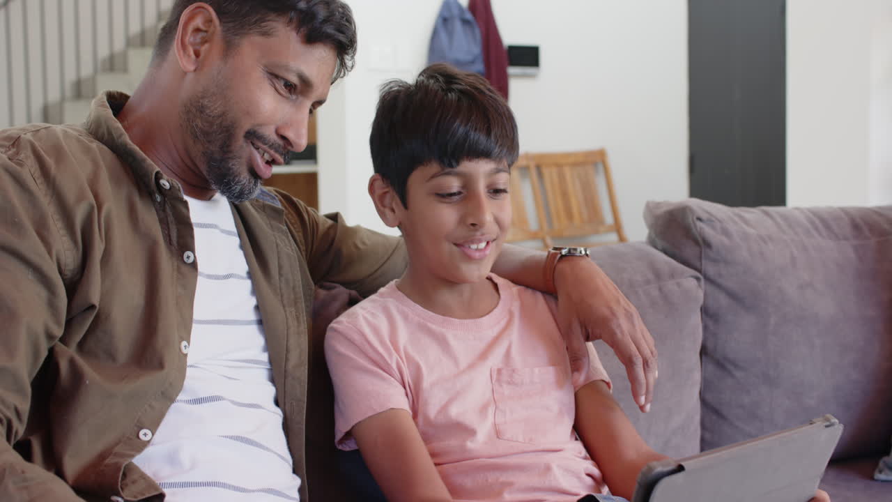 Smiling Indian father and son sitting on couch, enjoying quality time together
