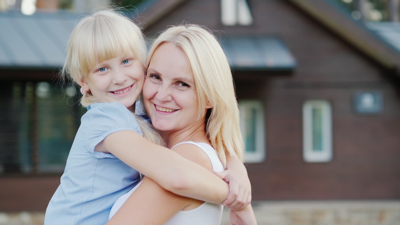 Porträt einer Mutter mit kleiner Tochter, die sich vor dem Hintergrund ihres neuen Zuhauses umarmen.