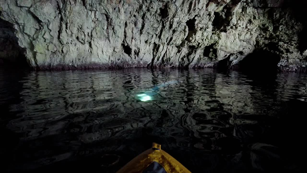 kayakista observando y moviéndose hacia un haz de luz en el agua dentro de una cueva marina, isla de vis, mar adriático, croacia