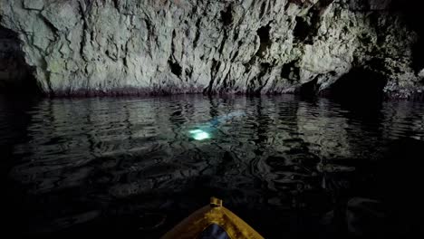 kayaker observing and moving towards a beam of light in the water inside a sea cave, vis island, adriatic sea, croatia