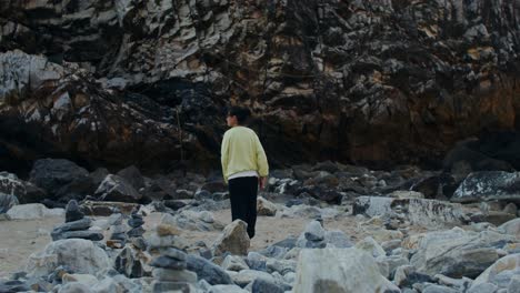 mujer caminando en una playa rocosa cerca de un acantilado