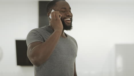 smiling black man talking phone at home. young guy standing with smartphone