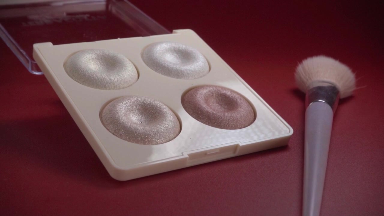 Close up of makeup highlighter palette with cosmetic brush featuring shimmering powder shades for facial highlighting beauty routine and makeup application