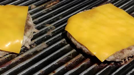 two homemade cheeseburgers cooking on a black grill