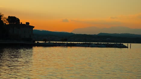 Golden-hour-sunset-on-a-lake,-calm-water-slowly-moving-with-orange-sky