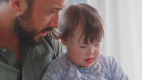 close up of father with down syndrome daughter reading book and laughing at home together