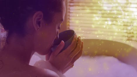 Animation-of-light-spots-over-caucasian-woman-drinking-coffee-and-taking-bath