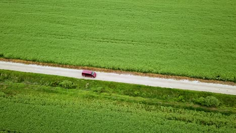 aerial landscape sideway shot of claret van driving on gravel road between green agricultural fields hungary europe