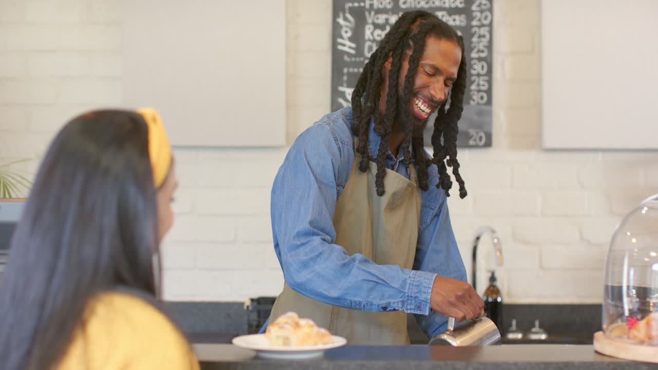 Afroamerikanische/r Barista gießt nach der Bestellung auf der Kaffeetheke gedämpfte Milch aus einem Krug