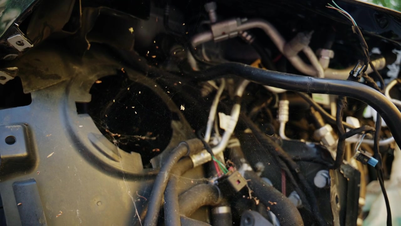 Detailed close up of dusty automotive wiring, hoses, and mechanical components inside a damaged vehicle