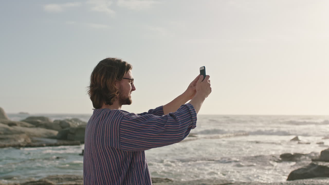 바다에서 전화를 사용하여 사진을 찍는 안경을 입은 젊은 남자의 초상화