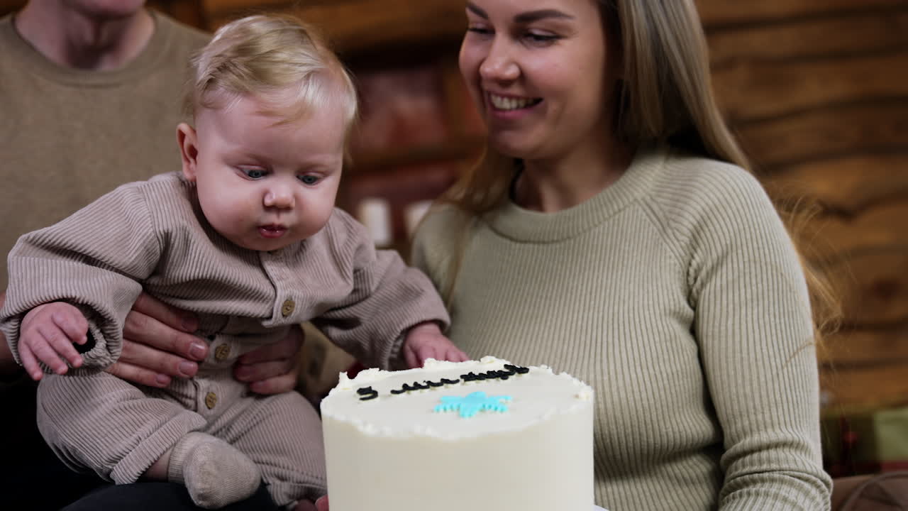 Adorable baby boy looking focused on the big cake in mom's hands. Family celebrates five months of their child's life.
