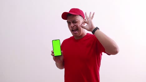 young handsome asian deliveryman showing green screen phone display and making okay hand gesture