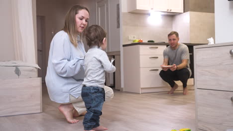 mother helping her baby to take his first steps in the living room at home 1