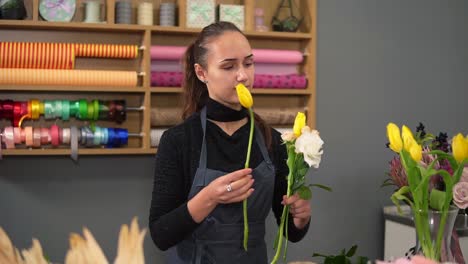 Slow-Motion-shot-of-young-female-florist-arranging-modern-bouquet-at-flowers-shot.-She-combines-creamy-roses-and-yellow-tulips