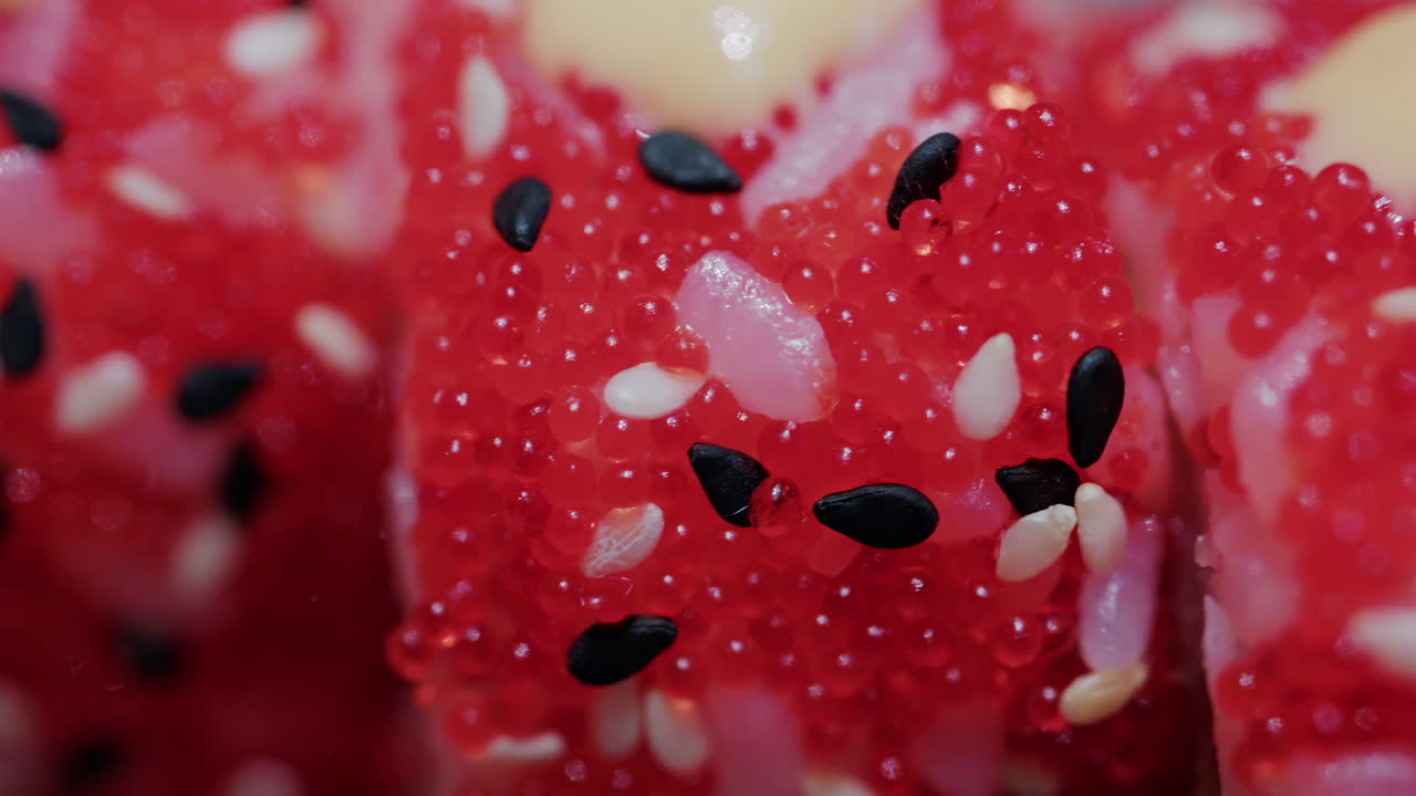 Close up of vibrant red sushi rolls topped with creamy sauce and sesame seeds, served on a ceramic plate