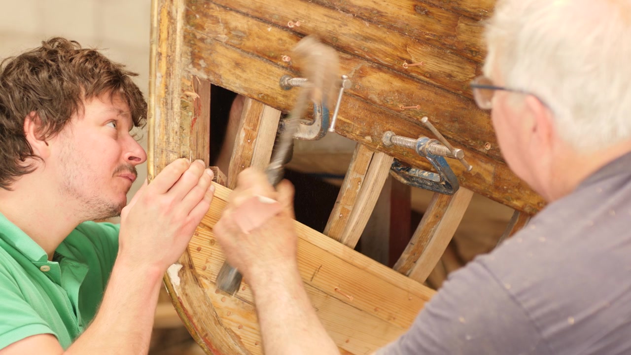 Apprendista e maestro d'ascia che fissano costole di quercia in una barca di legno a fasciame sovrapposto.