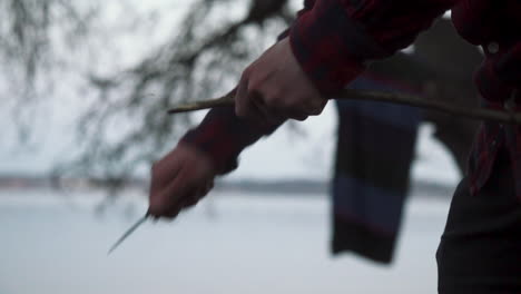 Man-carving-wood-in-a-forrest-water-in-background-slow-motion