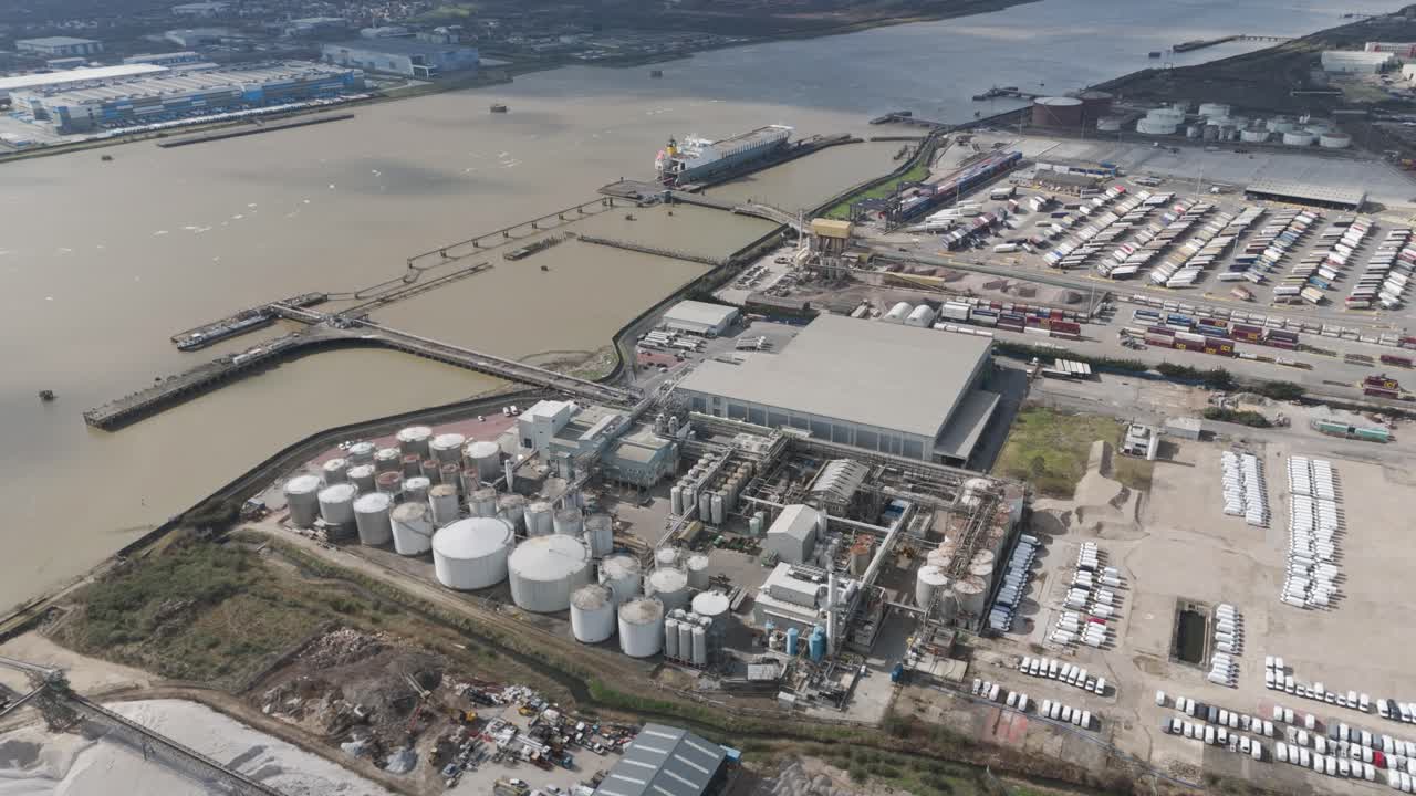 Aerial perspective of riverside oil storage facility with orderly cylinders, pipelines and service roads illustrating large-scale fuel logistics and energy distribution operations