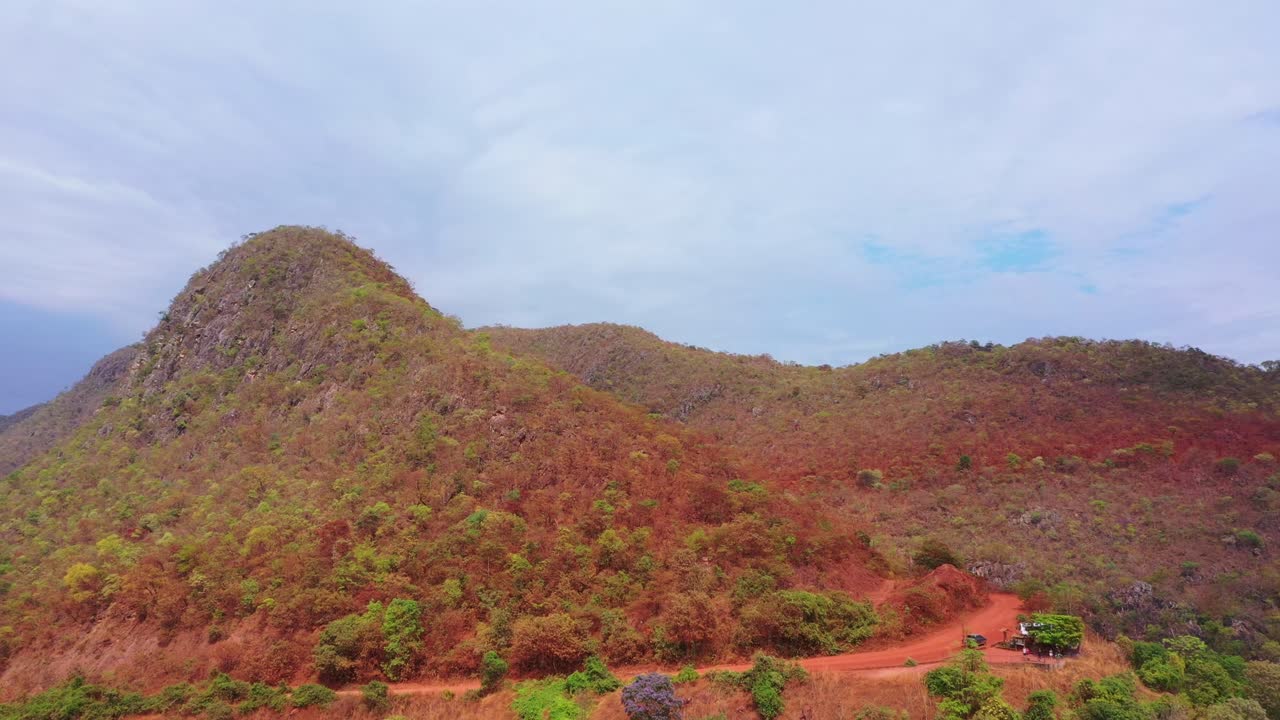 Un drone esegue un'ampia orbita attorno a una collina conica del Cerrado, mentre un camion 4x4 si trova sulla strada sterrata rossa alla sua base, sulla strada per Tocantins.