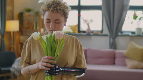 girl with prosthetic arm smelling fresh tulips at home
